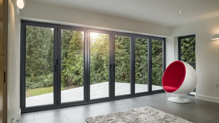 A set of grey Alumina aluminium bifold doors fully closed, providing a clear garden view from a modern indoor living space.