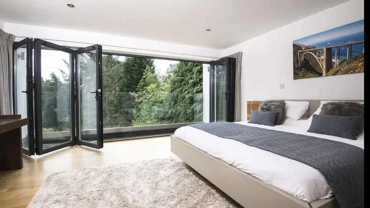 Alumina aluminium bifold doors in a modern bedroom, fully open to reveal a scenic outdoor view with a glass balcony.